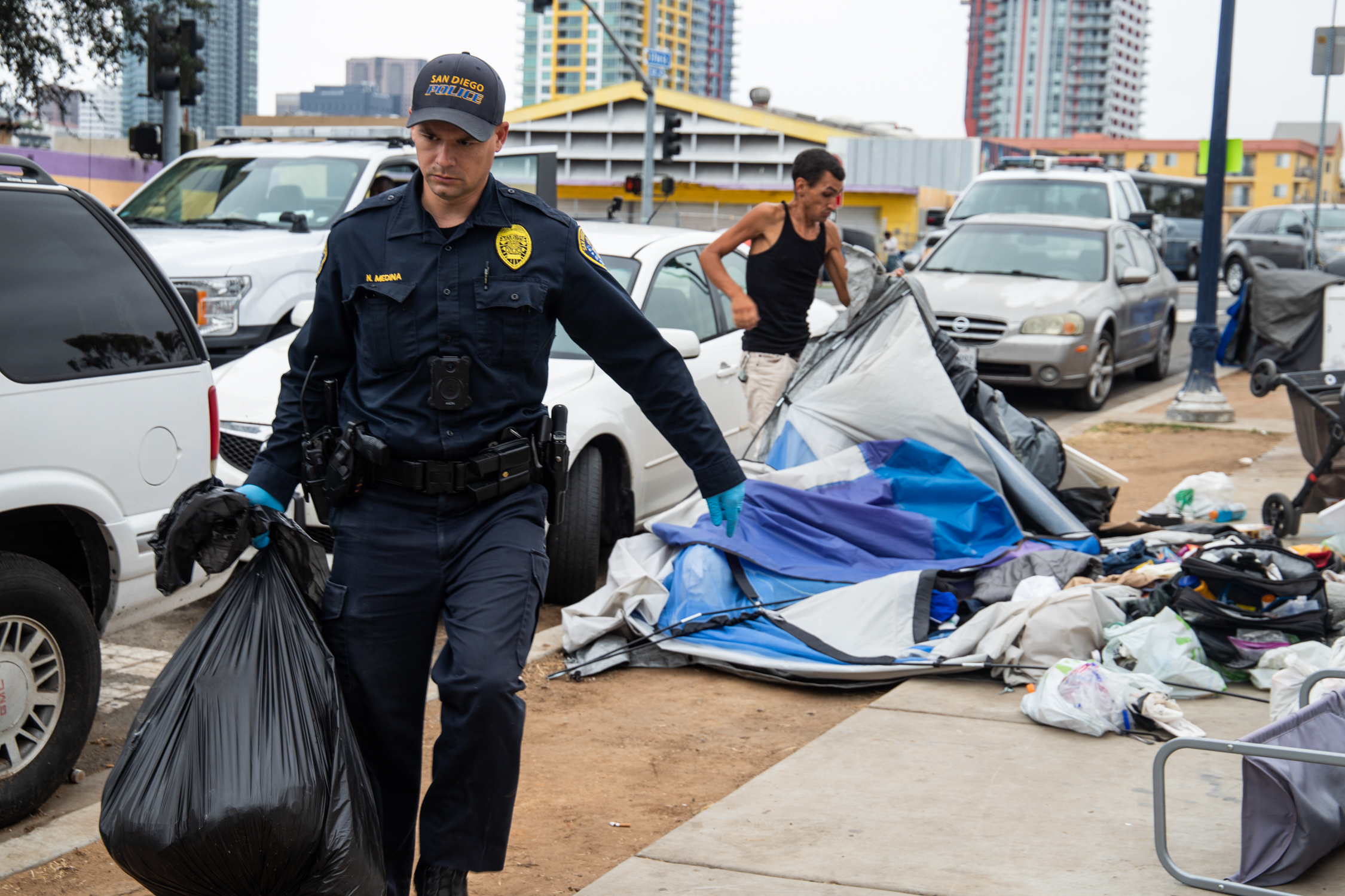 A San Diego Police officer picks up a bag of trash while conducting a homeless encampment sweep along 17th Street in downtown San Diego in August 2021. / File photo by Adriana Heldiz