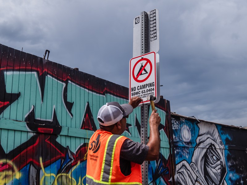 A city of San Diego worker puts a "No Camping" sign on Commercial Street in the outskirts of downtown on July 31, 2023.